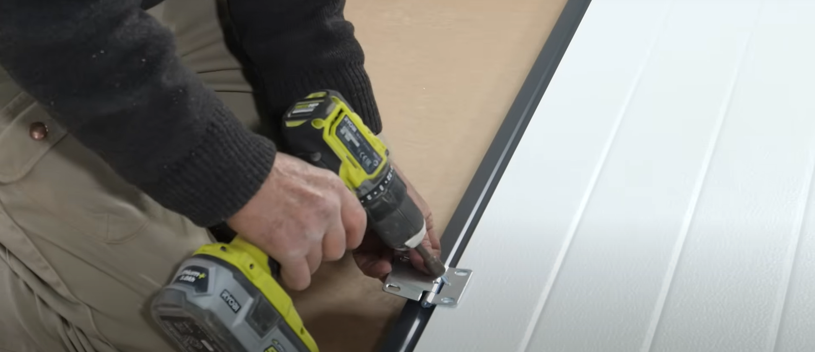 Technician performing garage door panel repair on a residential home, replacing a damaged metal panel with tools and safety gear